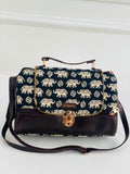 A navy blue handbag with a repeating cream elephant print on the flap and body, finished with dark brown leather trim, a top handle, and a gold-tone turn-lock clasp. The brand name 'Shagawa' is visible on a small leather patch.
