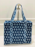 A blue and white patterned canvas tote bag with matching shoulder straps, displayed on a metal stand against a white wall.