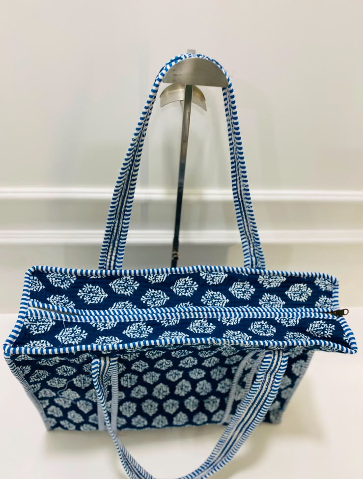 A blue and white patterned tote bag with matching shoulder straps, displayed on a stand against a plain white wall.